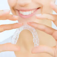 Manos sostienen un alineador transparente, mostrando cómo quitar Invisalign para una sonrisa perfecta.
