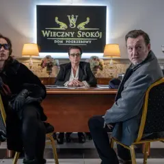 Trzy osoby siedzą w eleganckim biurze domu pogrzebowego. W tle logo "Wieczny Spokój". Scena z serialu "Minuta ciszy sezon 2".