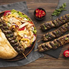 Un plateau de kebab et frites, avec des brochettes de viande grillée, du pain pita, une salade fraîche et des tomates. Un repas gourmand, attention à la calorie kebab frite !