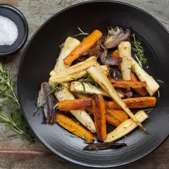 Légumes rôtis, carottes et panais, parsemés d'herbes. Un navet doré, tendre et savoureux, se mêle aux autres légumes sur l'assiette noire.