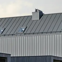Nowoczesny dach z blachy na rąbek, z oknami połaciowymi i kominem. Sprawdź blacha na rąbek cena m2.