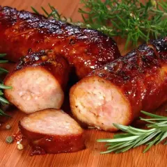 Soczysta kiełbasa z piekarnika, rumiana i aromatyczna, z gałązkami rozmarynu i ziarnami pieprzu na desce.