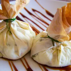 Dos saquitos de pasta filo rellenos, atados con hilo verde, reposan sobre un plato con un glaseado oscuro.