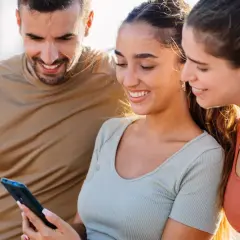 Trzech przyjaciół ogląda coś na telefonie. Uśmiechnięta dziewczyna, która trzyma telefon, może ukrywać zakochanie, gdy patrzy na ekran.