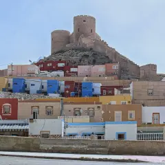 Casas de colores vibrantes se escalonan bajo la imponente fortaleza de **Sacromonte, Almería**.