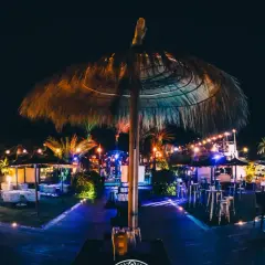 Noche vibrante en el chiringuito Macenas. Sombrillas de paja, luces de colores y mesas listas para disfrutar.