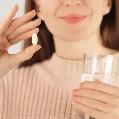 Kobieta trzyma tabletkę glicynianu magnezu i szklankę wody.