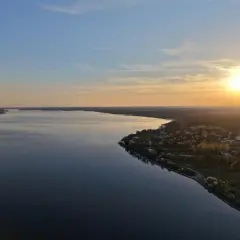 Zachód słońca nad Zalewem Sulejowskim. Woda odbija niebo, a na brzegu widać domki i drzewa. To idealne miejsce na relaks i podziwianie pięknych widoków, prawdziwe zalew sulejowski atrakcje.