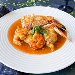 Rape en salsa con gambas y cigalas, servido en plato blanco con perejil fresco.