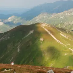 Widok na górzyste pasmo Tatr, gdzie zielone zbocza przecina kręta kopa kondracka trasa. W oddali widać kolejne pasma górskie.