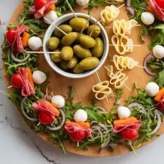 Kolorowe sałatki finger food na desce: szaszłyki z pomidorkami, mozzarellą, salami i warzywami, oliwki i ser.