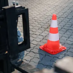 Ein orange-weißer Verkehrskegel steht auf einem gepflasterten Boden neben einem Gabelstapler. Man fragt sich, ob ein Staplerschein ablaufen kann.