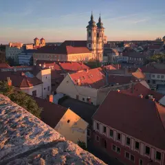 Widok na Eger z zamku o zachodzie słońca. Czerwone dachy, barokowa bazylika i wieże kościelne w złotym blasku.