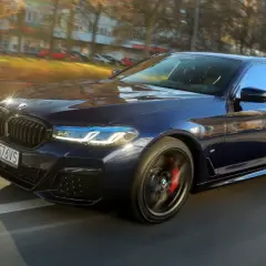 Ciemnoniebieskie BMW 540d sunie po drodze, odbijając jesienne słońce.