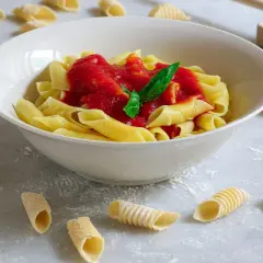 Garganelli alla contadina in una ciotola bianca, con pasta fresca sparsa sul piano di lavoro.