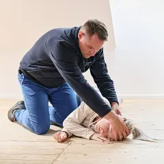 Mann übt stabile Seitenlage an einer liegenden Person. Die Person liegt auf der rechten Seite, der Kopf ist nach hinten geneigt.