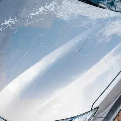 Krople wody i piany na masce srebrnego auta. Czy po woskowaniu płukać auto? Tak, aby uzyskać idealny połysk.