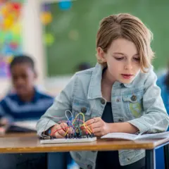 Ein Mädchen baut in einem Klassenzimmer an einem Stromkreis. Dies ist ein Beispiel für kompetenzorientierten Unterricht, bei dem Schüler praktische Fähigkeiten erlernen.