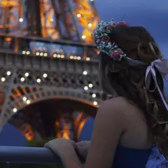 Ragazza con coroncina di fiori guarda la Torre Eiffel illuminata, un'atmosfera romantica perfetta per idee proposta di matrimonio.