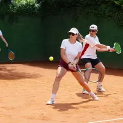 Trwa zacięta gra. Kobieta wykonuje tenisowe odbicie, a jej partner szykuje się do następnego uderzenia.