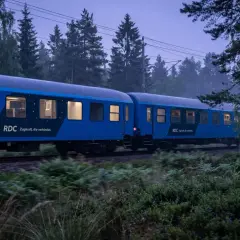 Blått nattåg från RDC passerar genom en skog i skymningen. Tåget är på väg mot Berlin, en resa som börjar i Sverige.