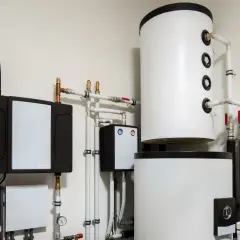Instalacja pompy ciepła z zasobnikami i rurami. Widoczny panel sterowania, który może wpływać na histerezę pompy ciepła, zapewniając optymalną pracę systemu.