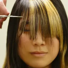 Fryzjerka przycina grzywkę w stylu birkin bangs. Dwukolorowe pasma opadają na twarz.