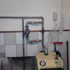 Montaż pompy CO w układzie otwartym. Widoczna instalacja hydrauliczna, czerwona pompa, zawory i fragment kotła.