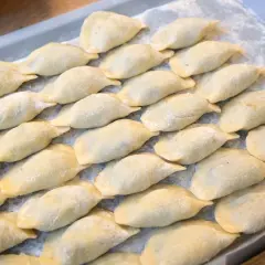 Ułóż surowe pierogi na tacy, posypane mąką, aby wiedzieć, jak przechowywać pierogi.