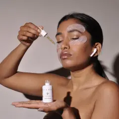 Donna applica siero per il contorno occhi disidratato. Patch idratanti e auricolari completano il rituale di bellezza.