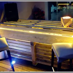 Bancone bar fai da te con pallet, illuminazione a LED e sgabelli. Un'idea creativa per un angolo bar moderno.