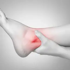 Mano che stringe una caviglia gonfia e dolorante, evidenziata in rosso.