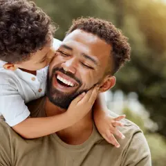 Un niño abraza a su padre, quien ríe feliz. Un momento tierno que inspira frases de padres a hijos para reflexionar sobre el amor.