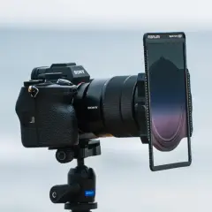 Aparat Sony z obiektywem i uchwytem na filtry do zdjęć. Tło rozmyte, morskie.