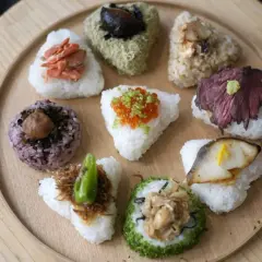 A colorful assortment of Japanese triangle food, including onigiri with salmon, beef, fish, and ikura, arranged on a wooden platter.