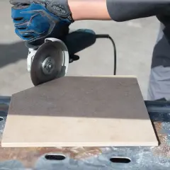 Mano guantata effettua un taglio piastrelle con flessibile, creando un angolo preciso su una piastrella beige.