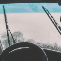 Conductor con gafas y barba, mira a través del parabrisas mojado. ¿Qué hacer si llueve y no anda el limpiaparabrisas?
