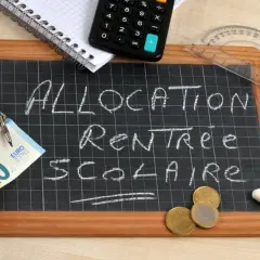 Tableau noir avec "Allocation Rentrée Scolaire" écrit à la craie. Un billet de 20 euros, des pièces, une calculatrice et un compas suggèrent un dépassement de plafond budgétaire.