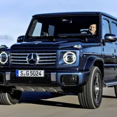 Ciemnoniebieski Mercedes G Klasa w ruchu. Kierowca uśmiecha się. Sprawdź aktualną mercedes g klasa cena.