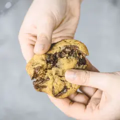Hände halten einen zerkrümelten Schokoladenkeks, der nach einem einfachen Cookies Rezept gemacht wurde.