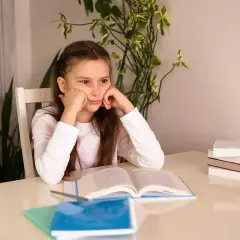 Zmęczona dziewczynka z podpartą głową na rękach, przed nią otwarte książki. Nauka jest trudna, zwłaszcza gdy jest się dyslektykiem.