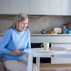 Donna anziana con le mani sull'addome, soffre di problemi di digestione. Le cause possono essere molteplici.