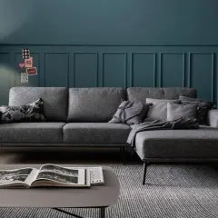 Ein modernes Wohnzimmer mit einem grauen Sofa, das mit Kissen und einer Decke dekoriert ist. Ein Stehlampen-Design und eine Zimmerpflanze runden das Bild ab.