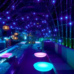 Interni di un night club a Valencia, con luci blu e viola, tavoli luminosi e sedute comode.