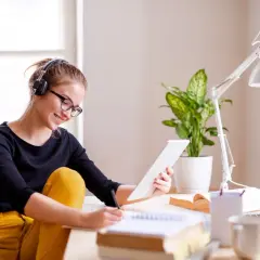 Junge Frau mit Kopfhörern und Brille lernt am Tablet für ihr **vollzeit studium**. Sie schreibt Notizen in ein Heft.