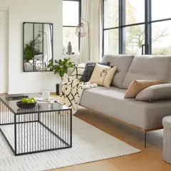 Salon à la décoration épurée et moderne : canapé gris, table basse noire, meuble blanc, miroir, plaid et coussins graphiques.