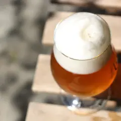 Ein Glas Bier mit cremigem Schaum steht auf Holz. Der goldene Farbton lässt den Unterschied zwischen Pils und Helles erahnen.