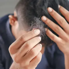 Persona preocupada revisa un mechón de pelo quebradizo, buscando posibles causas.