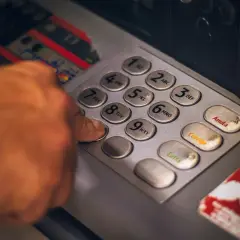 Dłoń wpisuje PIN na klawiaturze bankomatu, symbolizując dostęp do usług finansowych i **open banking**.