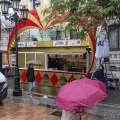 Preparativos para las fiestas de San Mateo en Oviedo. Un puesto de comida y bebida con decoración festiva, gente con paraguas y un furgón blanco.